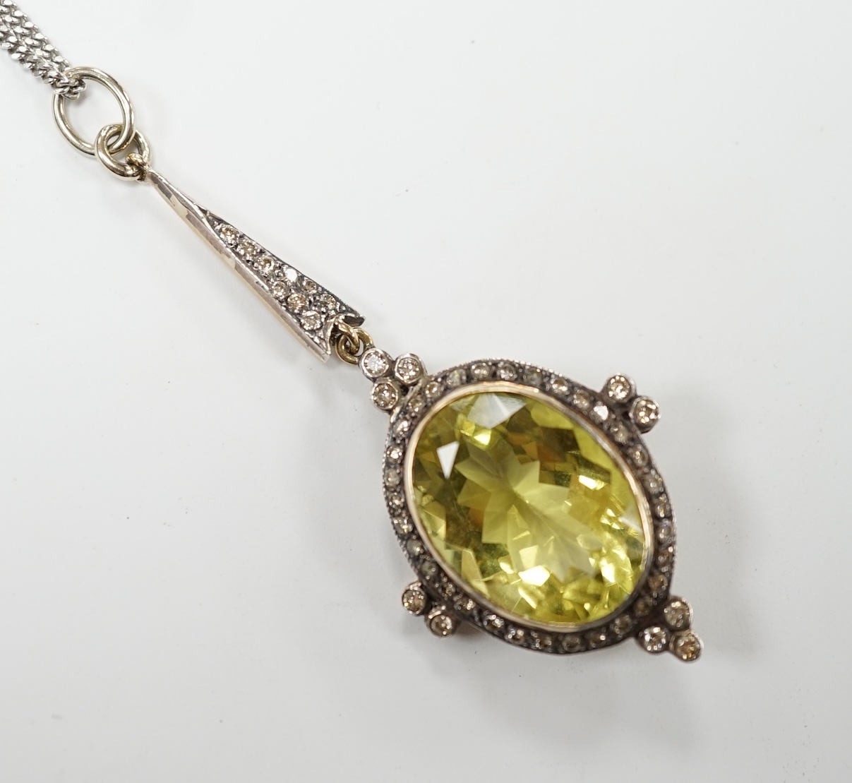A late Victorian yellow metal and single stone oval cut citrine set drop pendant, with diamond set border and bale, 53mm, on a later 375 white metal chain, 50cm, gross weight 11.2 grams. Good condition.